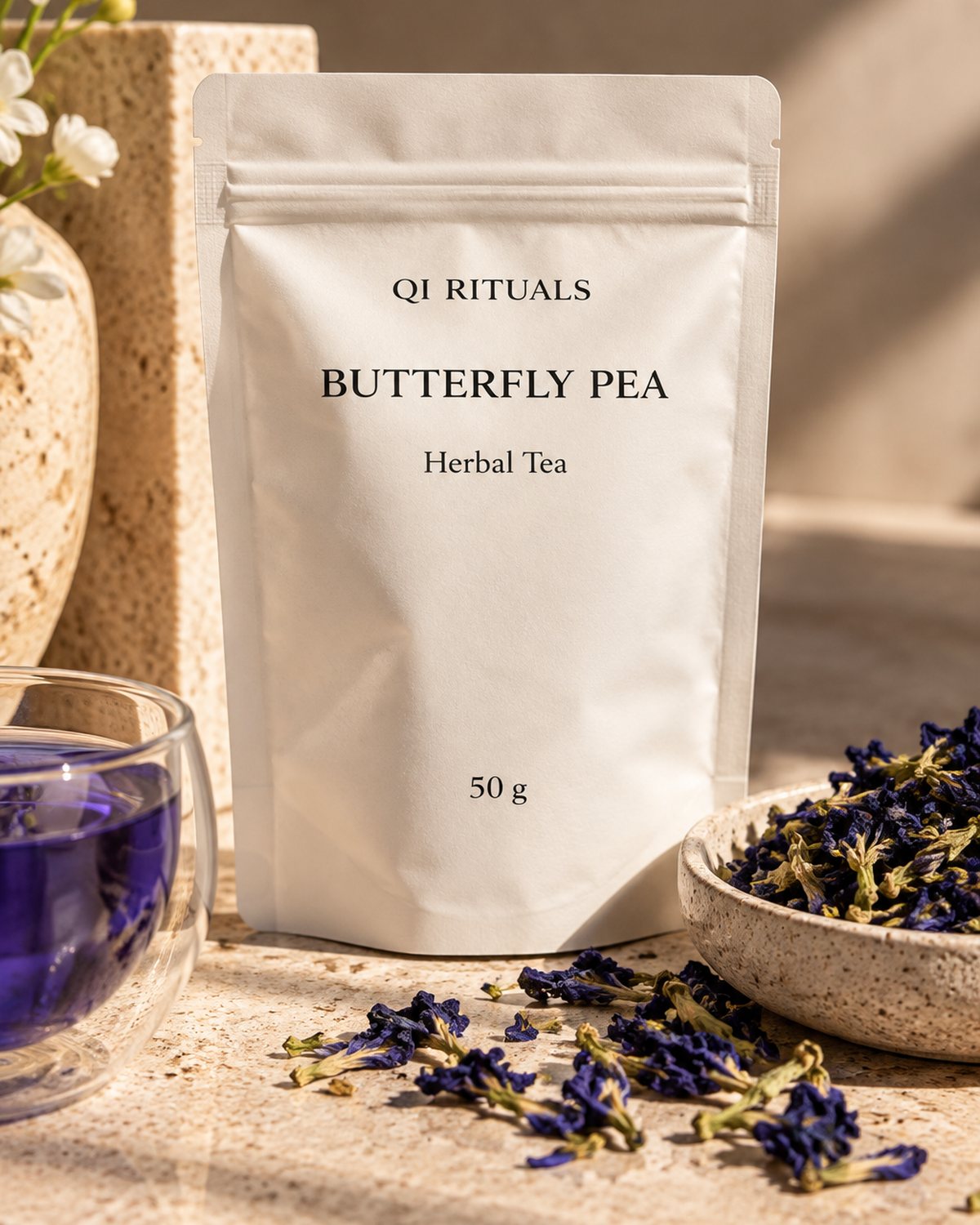 Butterfly pea herbal tea pouch beside a glass of deep blue tea and dried flowers